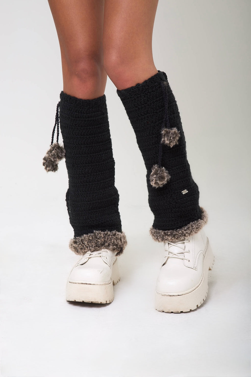 Front view of black Not Your Baby legwarmers with pom-pom details worn over white sneakers