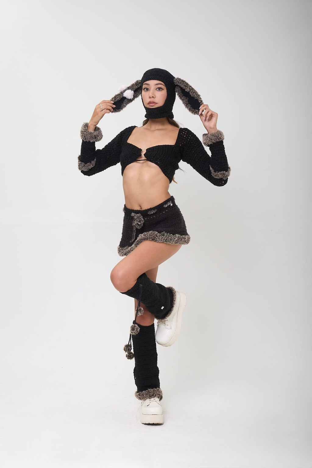 Model wearing black Not Your Baby legwarmers as part of a black outfit with fur accents on a white background