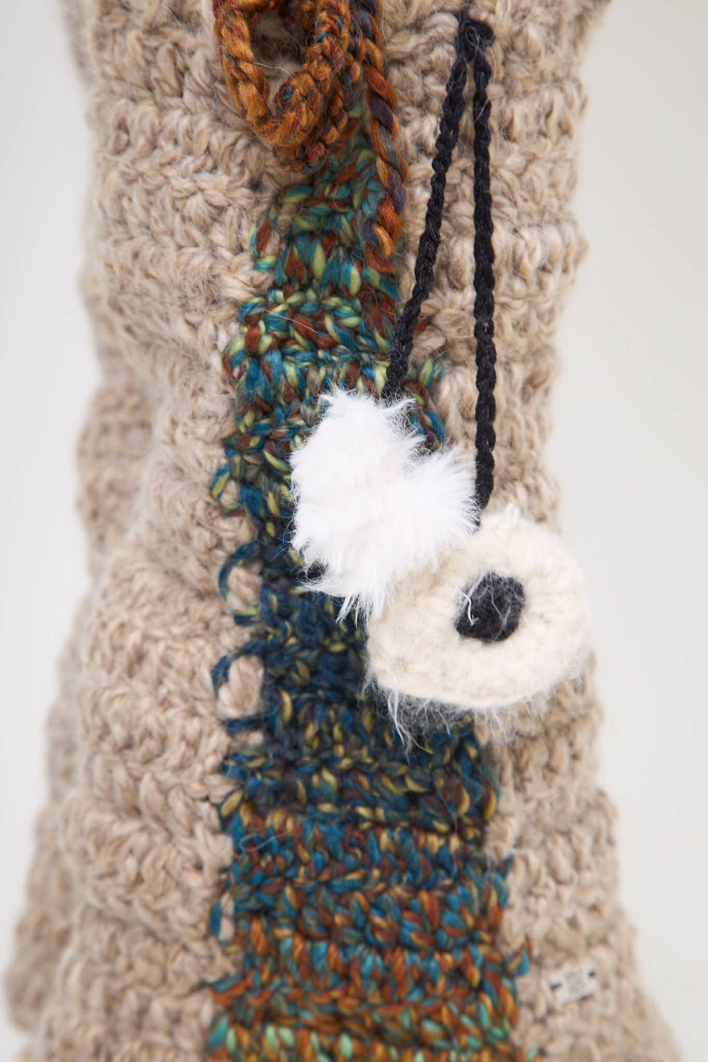 Close-up of evil eye and pom pom detail on crochet leg warmers